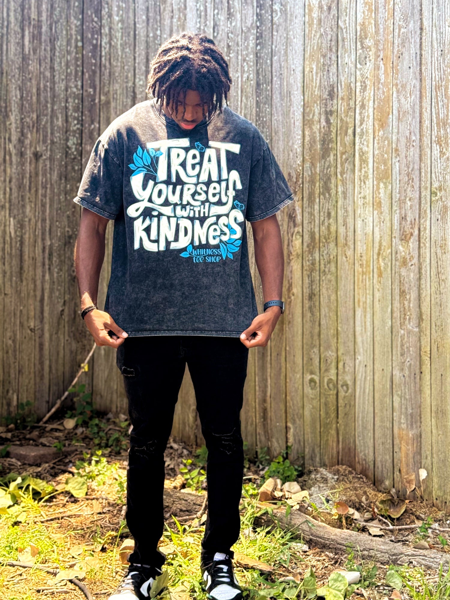 Person wearing a t-shirt with a motivational quote standing in front of a wooden fence.
